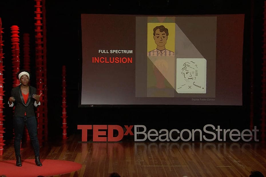 Black MIT grad student Joy Buolamwini standing on stage giving TedTalk speech with screen in back drop stating "Full Spectrum Inclusion" and graphic included